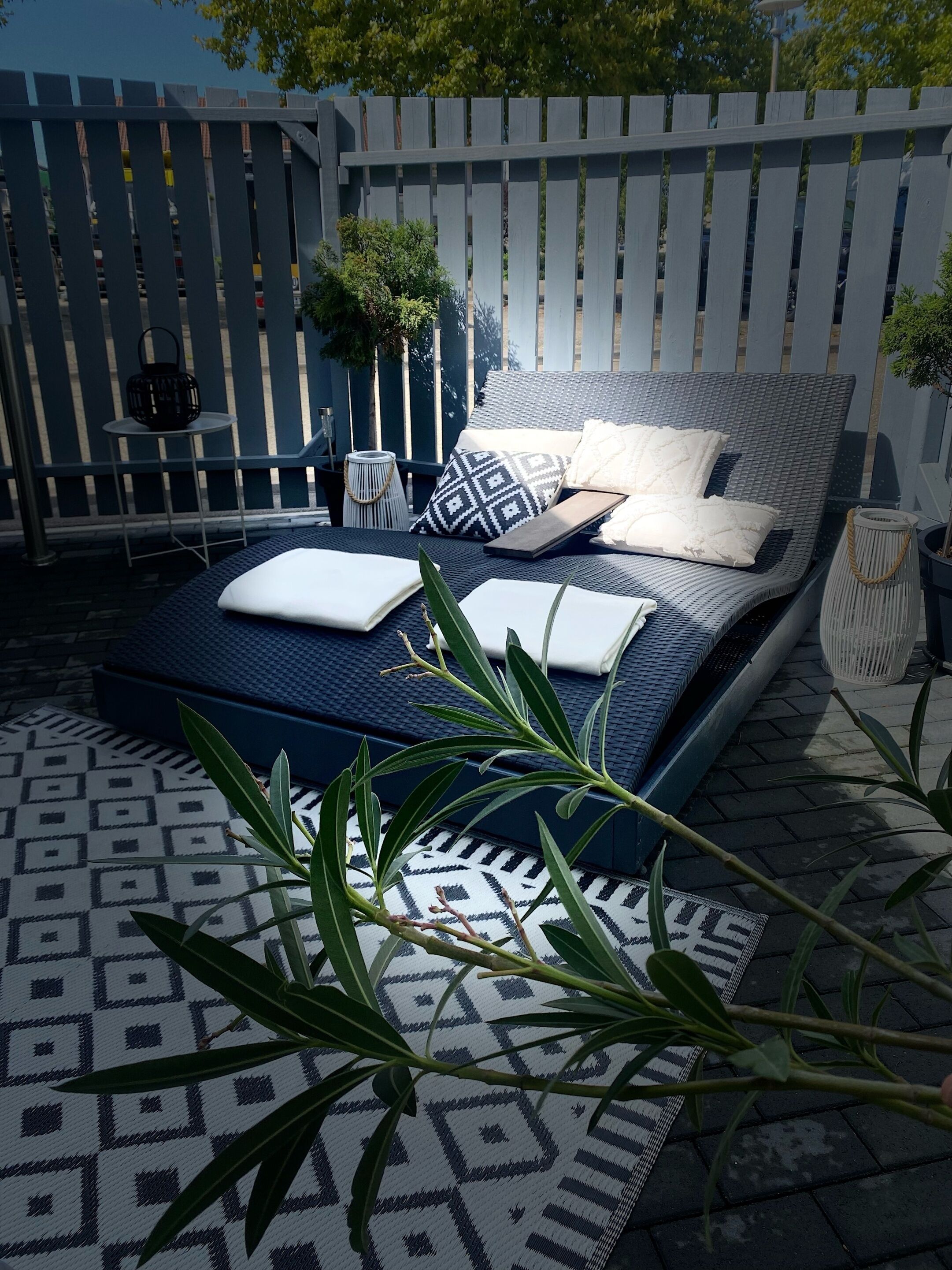 A bed with a patterned mattress, pillows, and a bedside table with a lamp and a small plant.