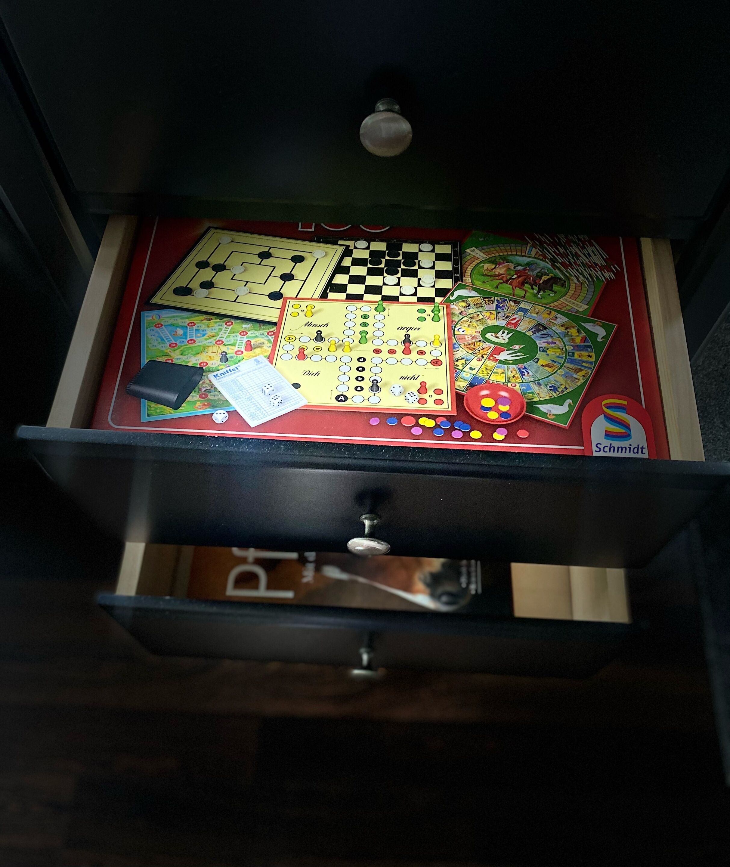 A drawer containing various board games, including checkers, chess, and a game with a colorful board.