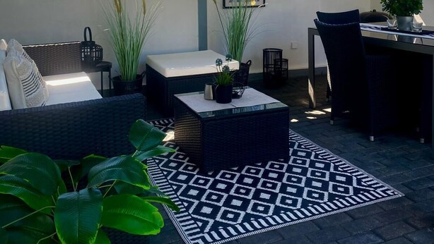An outdoor patio area with a covered seating area, a dining table, and various potted plants.
