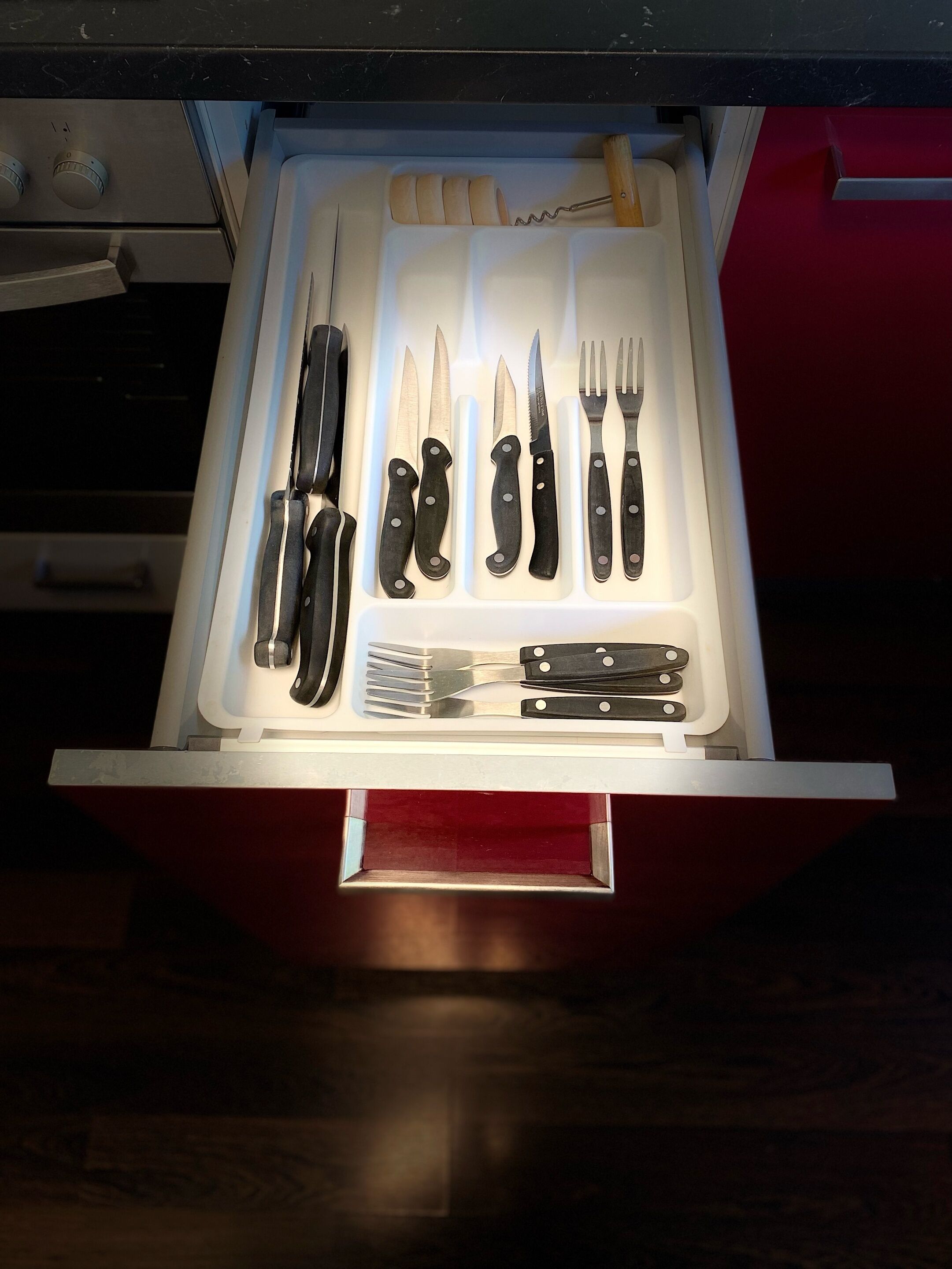 Un tiroir contenant divers ustensiles de cuisine, notamment des couteaux, des fourchettes et un tire-bouchon.