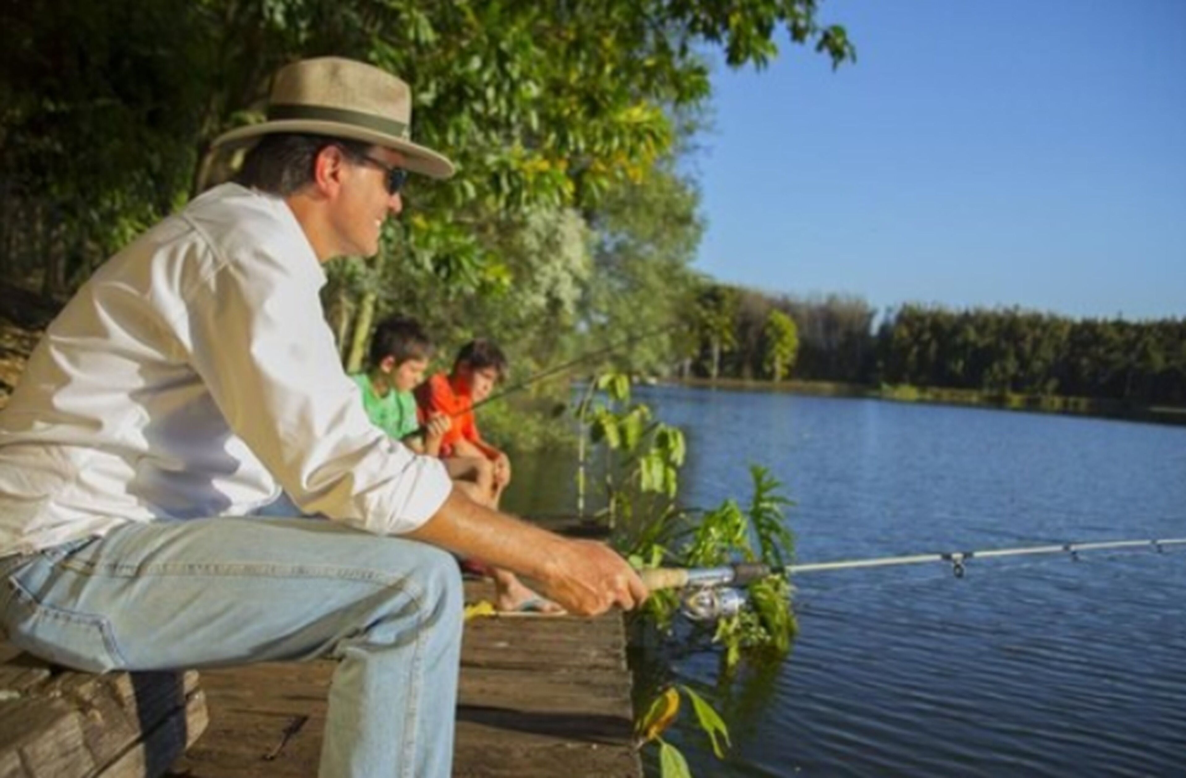 A person fishing by a calm lake with trees in the background.