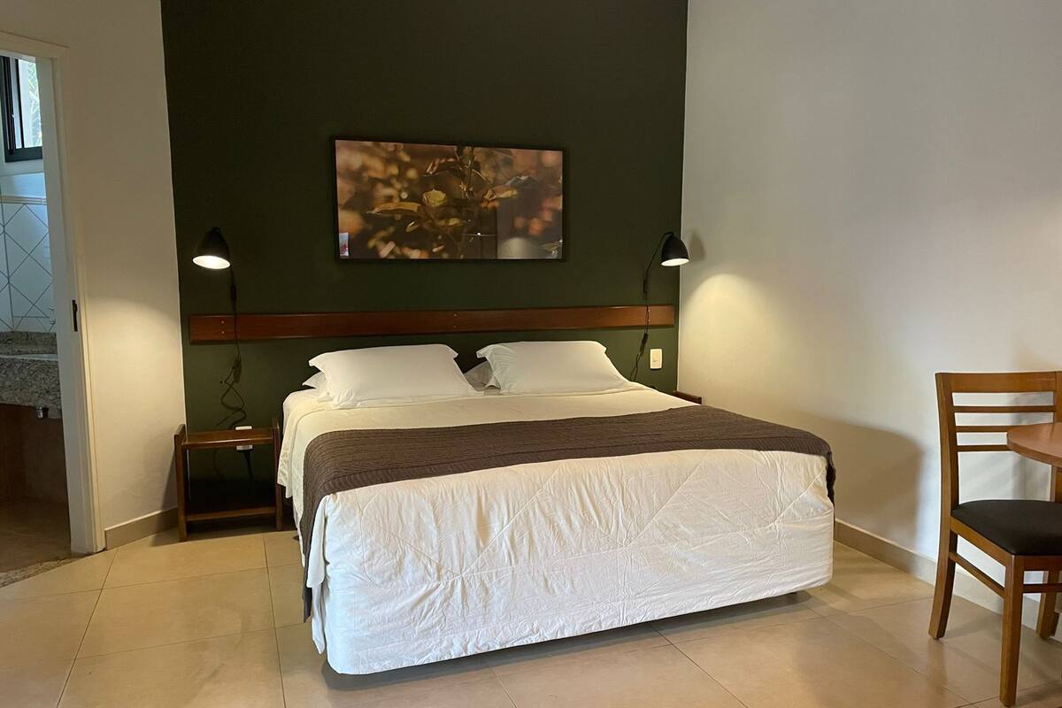 A neatly made bed with a white duvet and a brown throw blanket, a wooden headboard, two bedside lamps, and a framed picture on the wall.