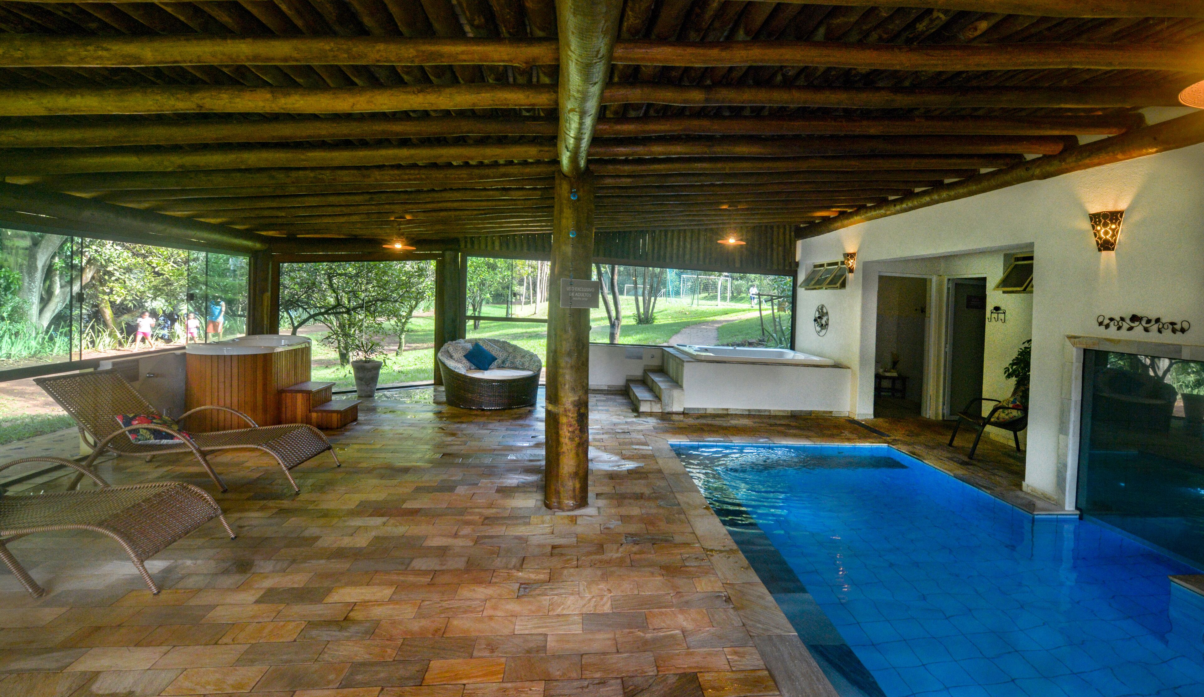 Une piscine intérieure dotée d’un plafond en bois, d’un jacuzzi et d’un espace détente avec des meubles en osier.