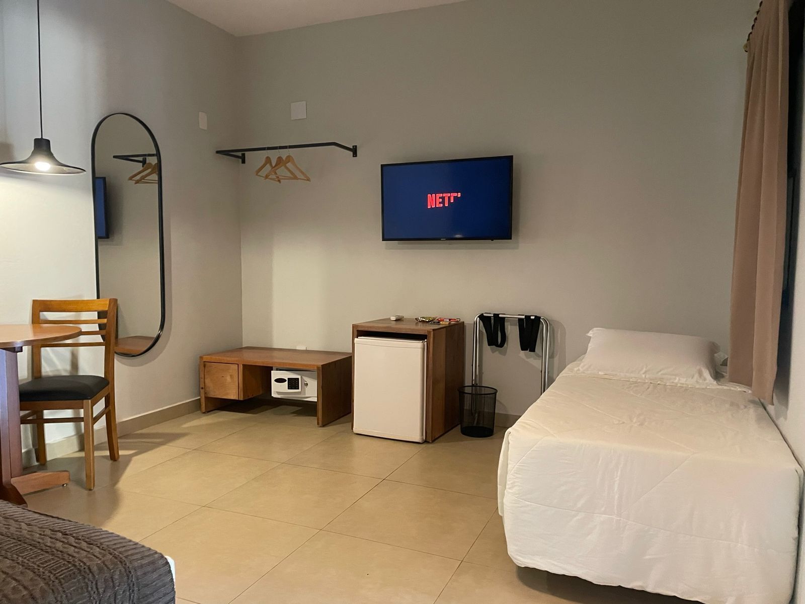 Une chambre d’hôtel comprenant un lit, un bureau avec une chaise, un petit réfrigérateur, un téléviseur fixé au mur et un miroir.