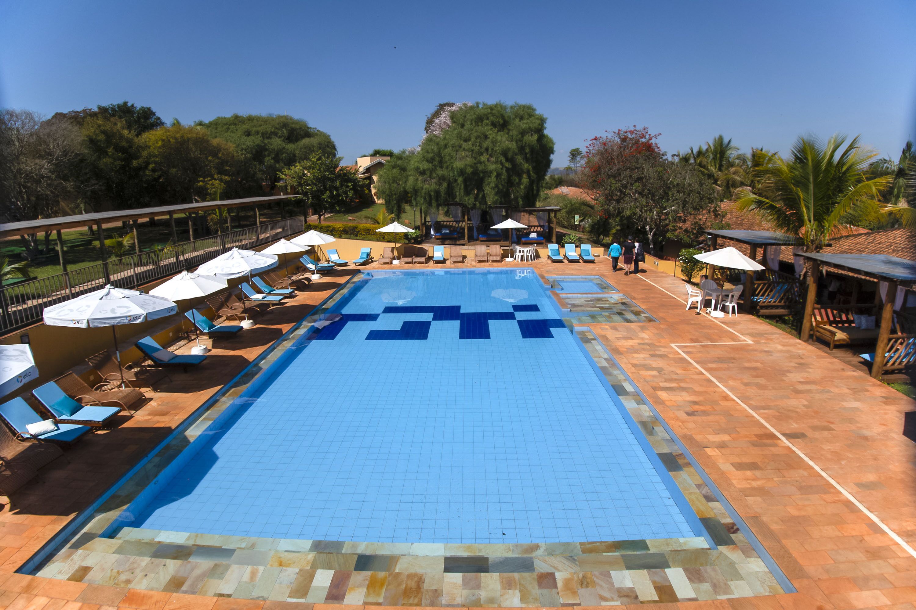 Una piscina con azulejos azules, rodeada de sillas de descanso y sombrillas.