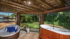 Un área de spa con un jacuzzi, una silla de descanso de mimbre y vistas a una piscina y jardín.