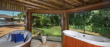 A spa area with a hot tub, a wicker lounge chair, and a view of a pool and garden.
