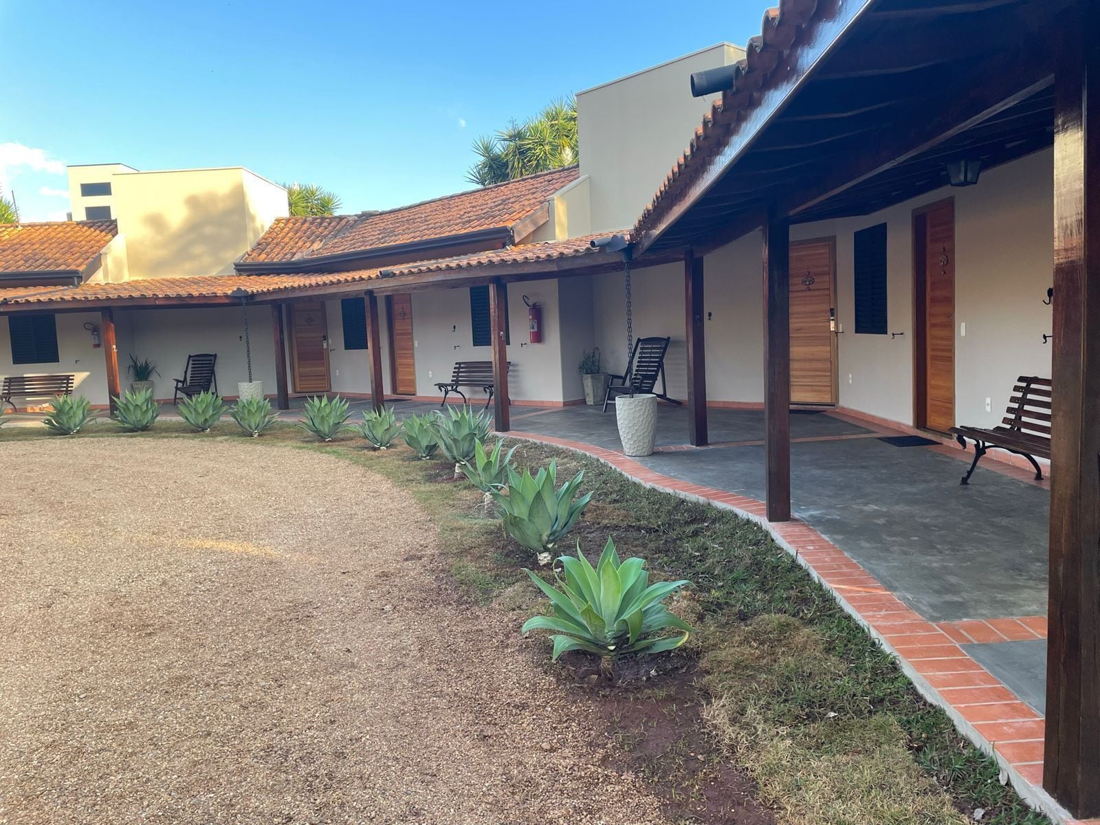 Un patio con un camino de grava, bancos y macetas.