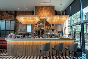 Zona de bar con pared de ladrillo, luces colgantes y mostrador con taburetes.