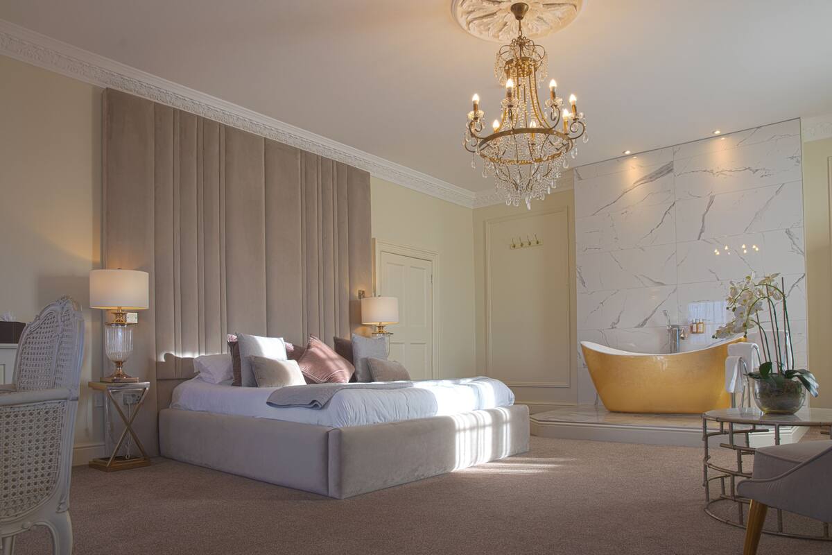 Une chambre spacieuse avec un grand lit, une baignoire et un lustre.