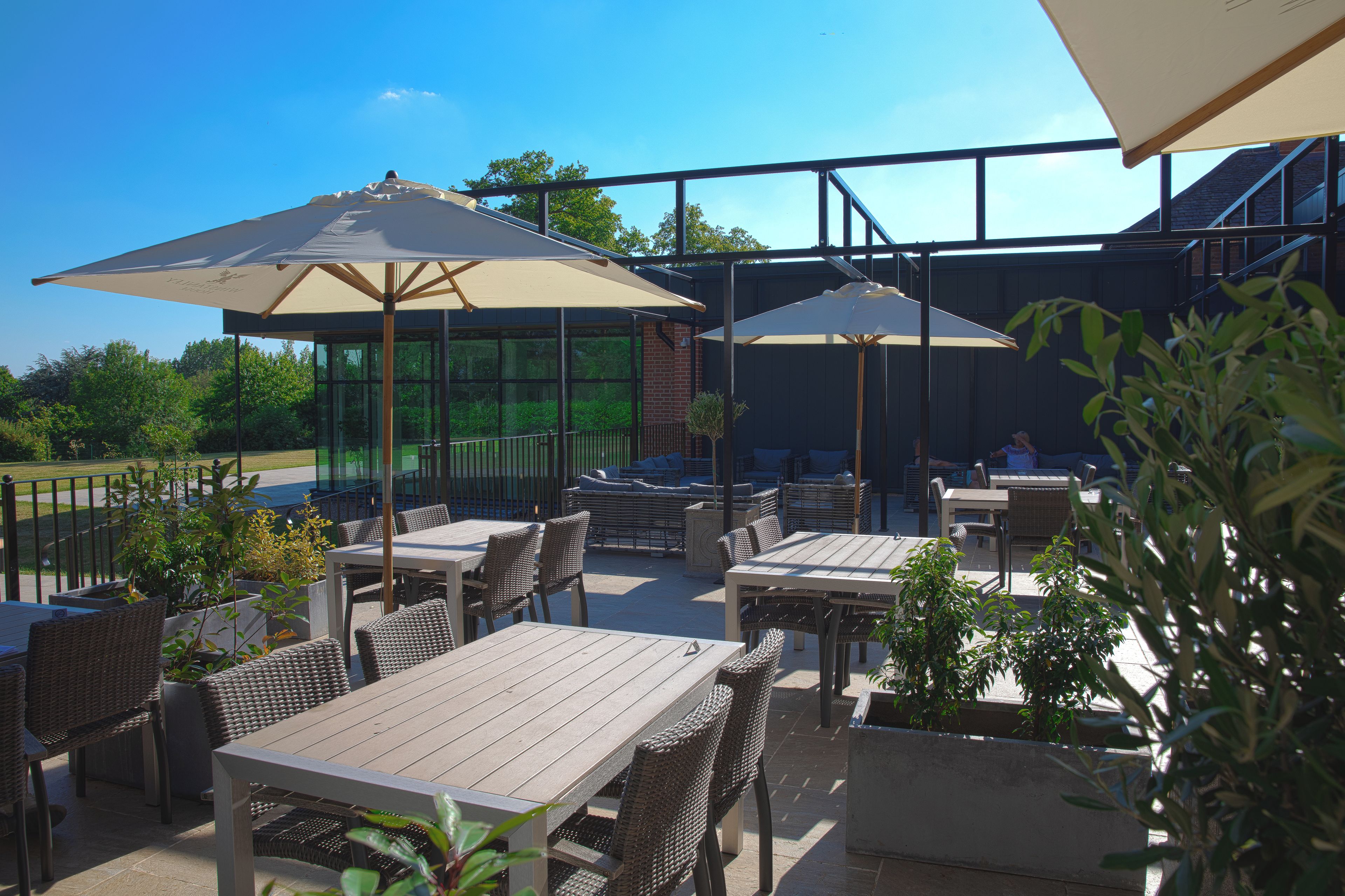 Ein Außenbereich mit Terrasse, Tischen, Stühlen, Sonnenschirmen und Kübelpflanzen.