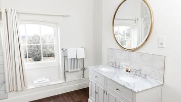A bathroom with a double sink, a large mirror, a towel rack, and a window with curtains.