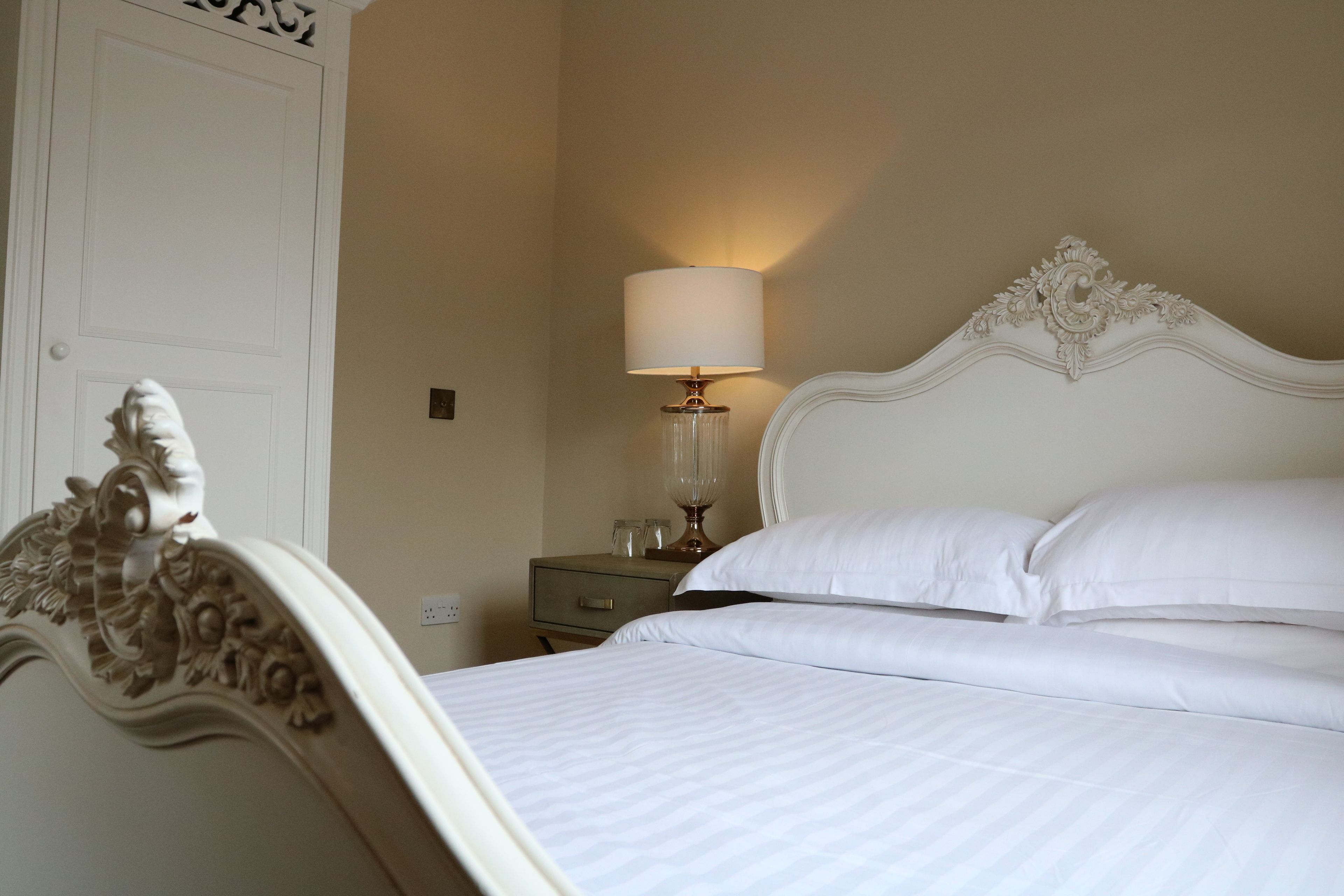 A neatly made bed with white linens, a bedside lamp, and a nightstand with a glass decanter.