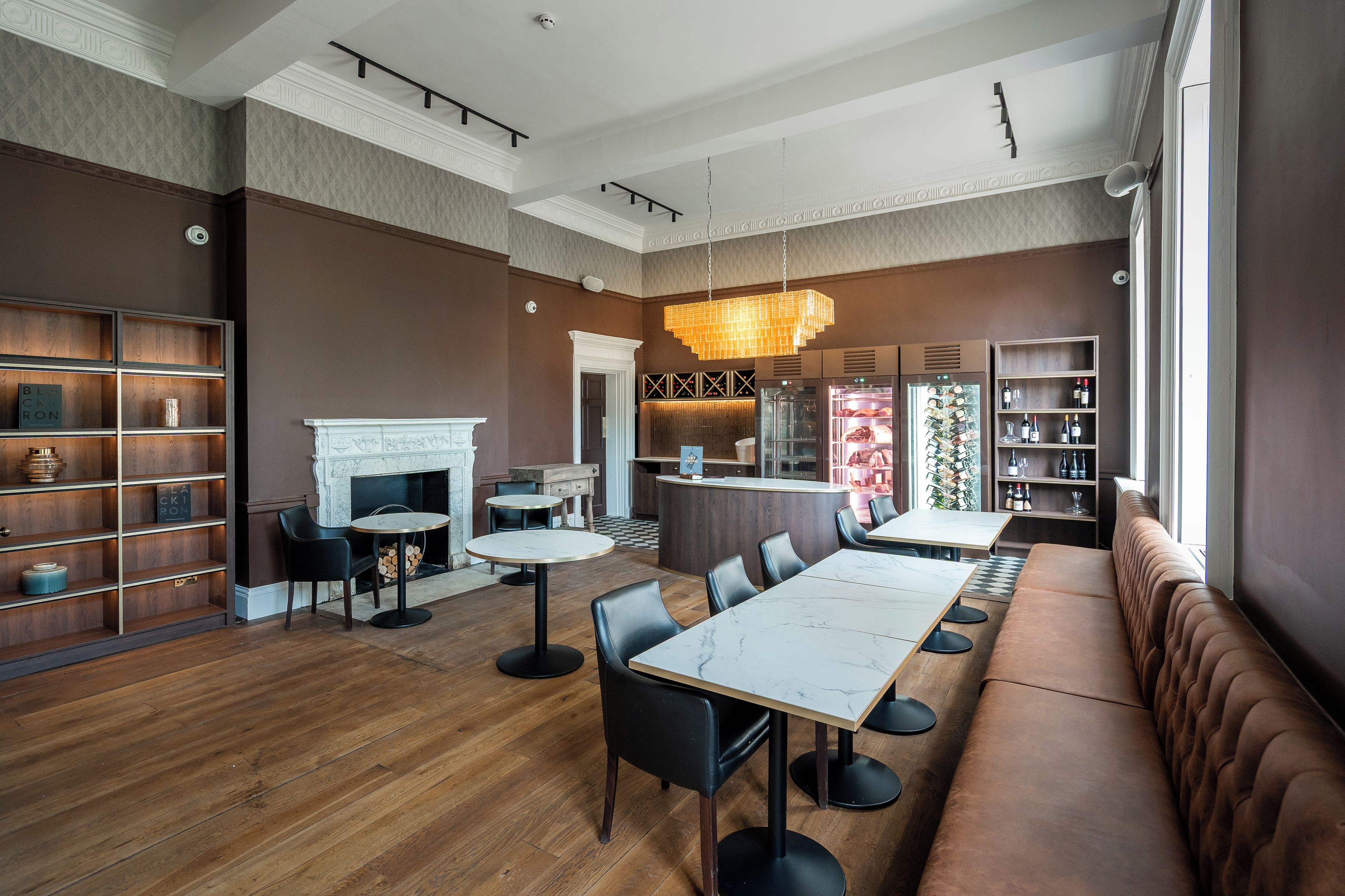 A modern restaurant interior with a long communal dining table, black leather seating, and a fireplace.