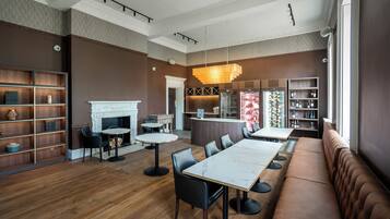 A modern restaurant interior with a long communal dining table, black leather seating, and a fireplace.