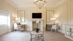 A spacious room with a large chandelier, a fireplace, a television mounted on the wall, and a desk with a chair. - Winstanley House (Leicester)