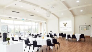 A spacious conference room with multiple tables and chairs, large windows, and a chandelier. - Winstanley House (Leicester)