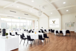 A spacious conference room with multiple tables and chairs, large windows, and a chandelier.