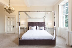 A four-poster canopy bed with a tufted headboard, bedside tables with lamps, and a chandelier. - Winstanley House (Leicester)