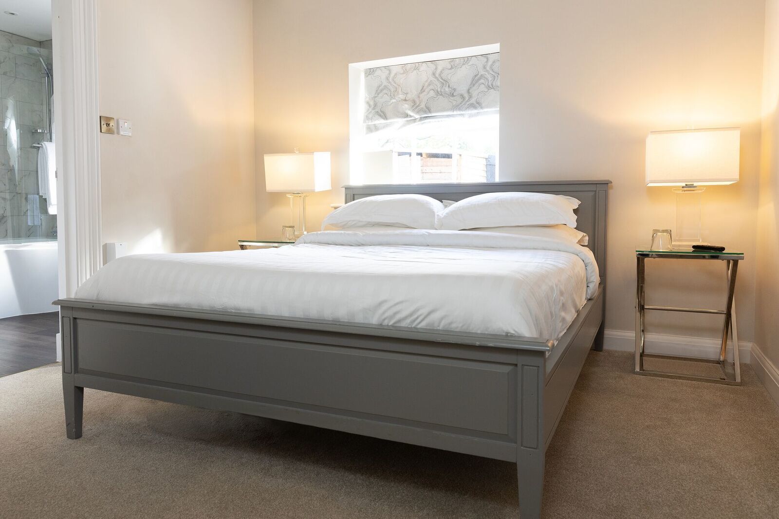 A bedroom with a bed, two bedside lamps, a window with a view, and a marble-patterned wall art piece.