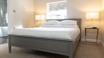 A bedroom with a bed, two bedside lamps, a window with a view, and a marble-patterned wall art piece.