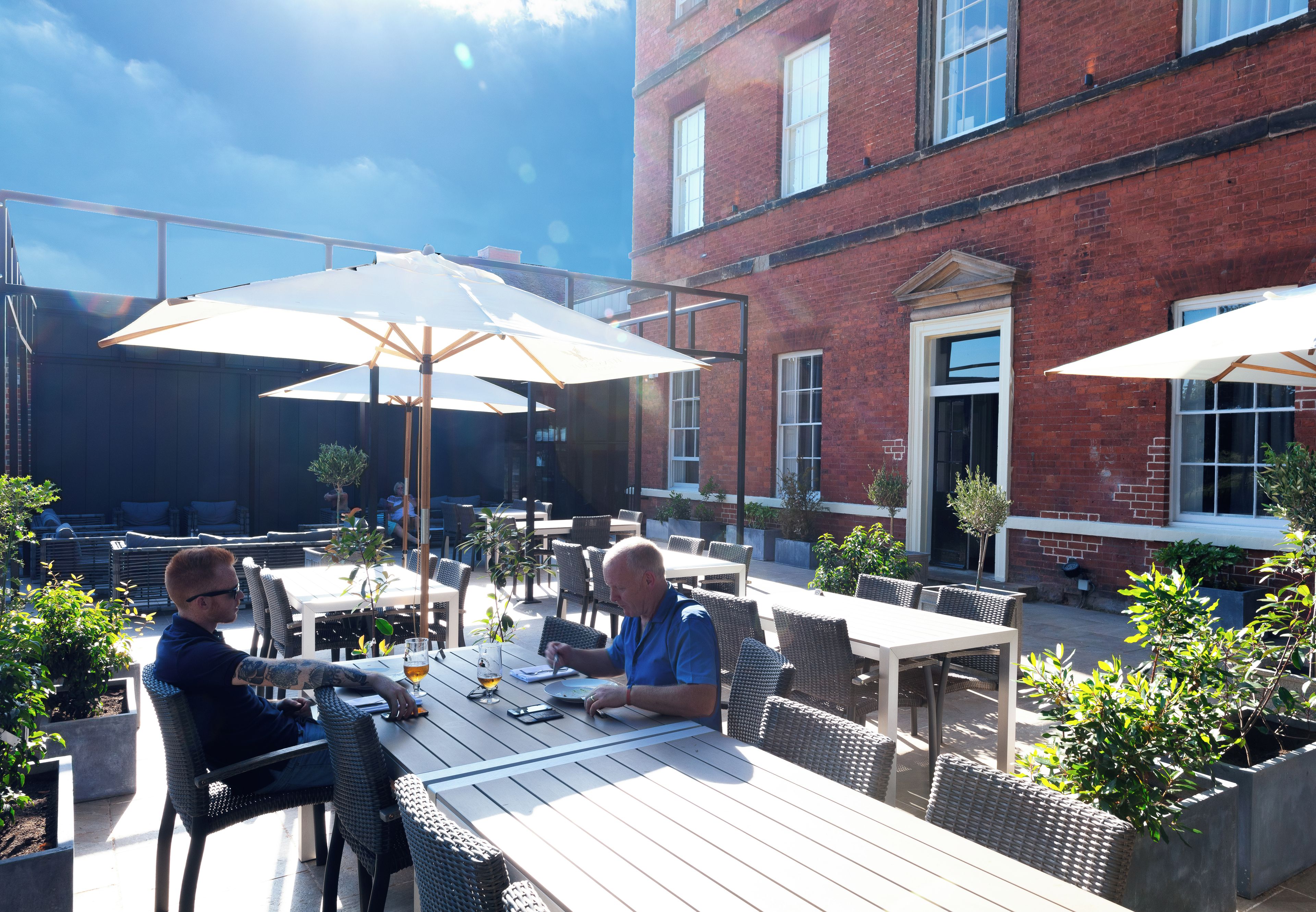 An outdoor seating area with tables and chairs, umbrellas, and potted plants.