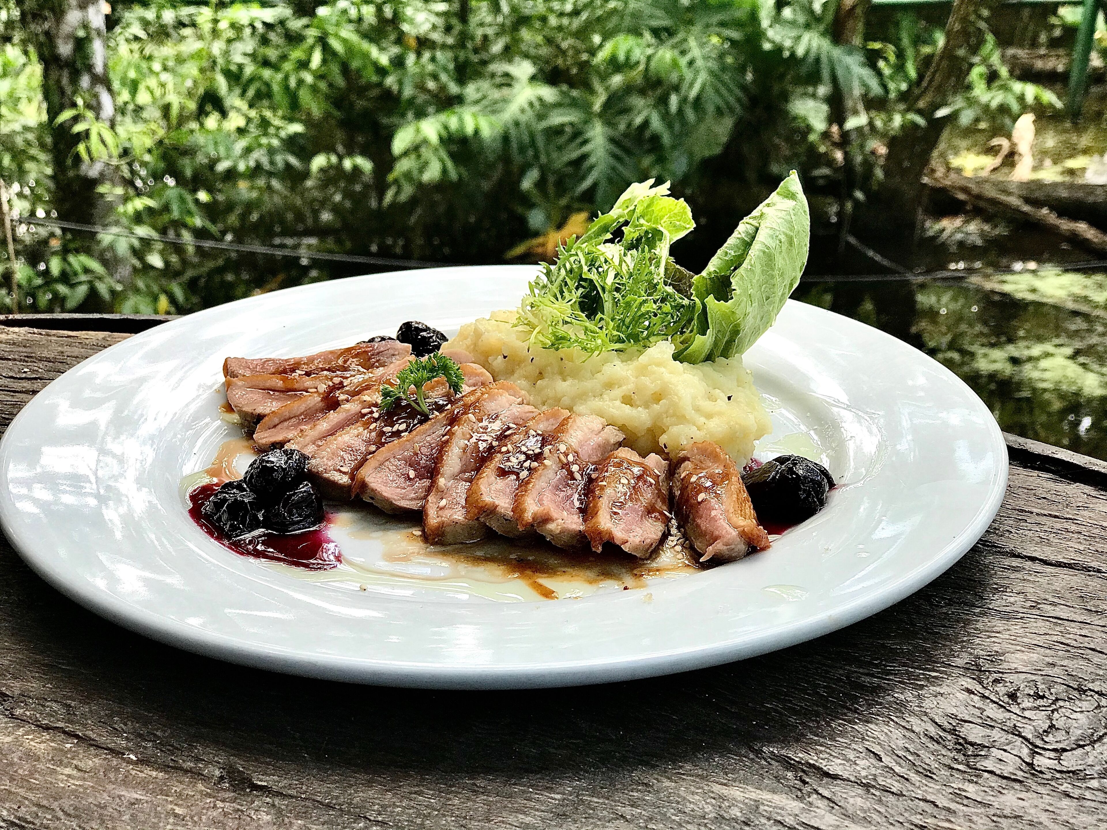 A plate of food with sliced meat, mashed potatoes, and greens, served on a white plate.