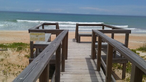A wooden boardwalk leading to a beach with a sign indicating it is property of Ocean Crest. - Ocean Crest Motel (Ormond Beach)
