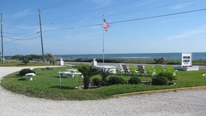 A grassy area with a flagpole, a bench, and a signboard indicating a vacancy at Ocean Crest. - Ocean Crest Motel (Ormond Beach)