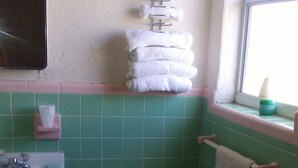 A bathroom with a toilet, sink, and stacked towels on a rack. - Ocean Crest Motel (Ormond Beach)