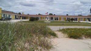 A motel with a row of single-story buildings, each with a yellow door and a small front yard. - Ocean Crest Motel (Ormond Beach)