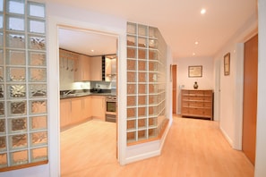 A modern kitchen with wooden cabinets, a built-in oven, and a glass partition. - Town or Country - Greenwich Apartments (Southampton)