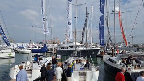 Ein Yachthafen mit mehreren angedockten Booten, einige davon mit Flaggen, und Personen auf und um die Boote.