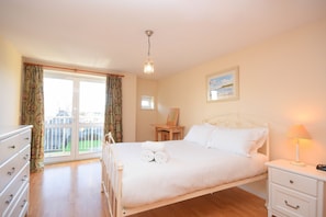 A bedroom with a bed, a nightstand, a dresser, a window with curtains, and a painting on the wall. - Town or Country - Greenwich Apartments (Southampton)