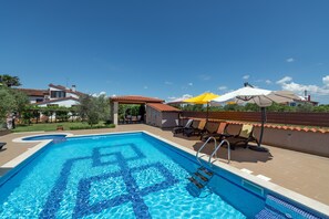 Una piscina con diseño de azulejos, sillas de descanso, sombrillas y un cielo azul despejado.