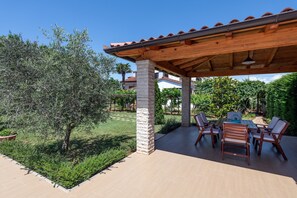 An outdoor patio with a wooden pergola, a table with chairs, and a well-maintained garden. - Apartments Neva (Pula)
