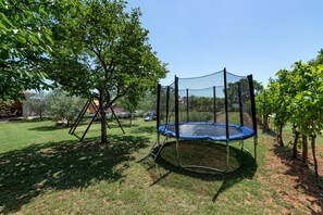 A trampoline in a backyard with a tree and a house in the background. - Apartments Neva (Pula)