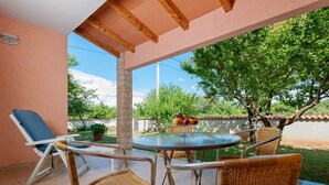 A covered patio with a round table and wicker chairs, a lounge chair, and a fruit basket. - Apartments Neva (Pula)