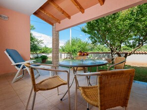 A covered patio with a round table and wicker chairs, a lounge chair, and a fruit basket. - Apartments Neva (Pula)