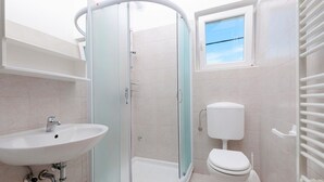 A modern bathroom with a glass-enclosed shower, a white sink, and a toilet. - Apartments Neva (Pula)