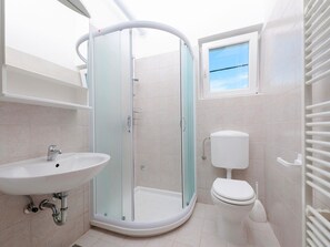 A modern bathroom with a glass-enclosed shower, a white sink, and a toilet. - Apartments Neva (Pula)
