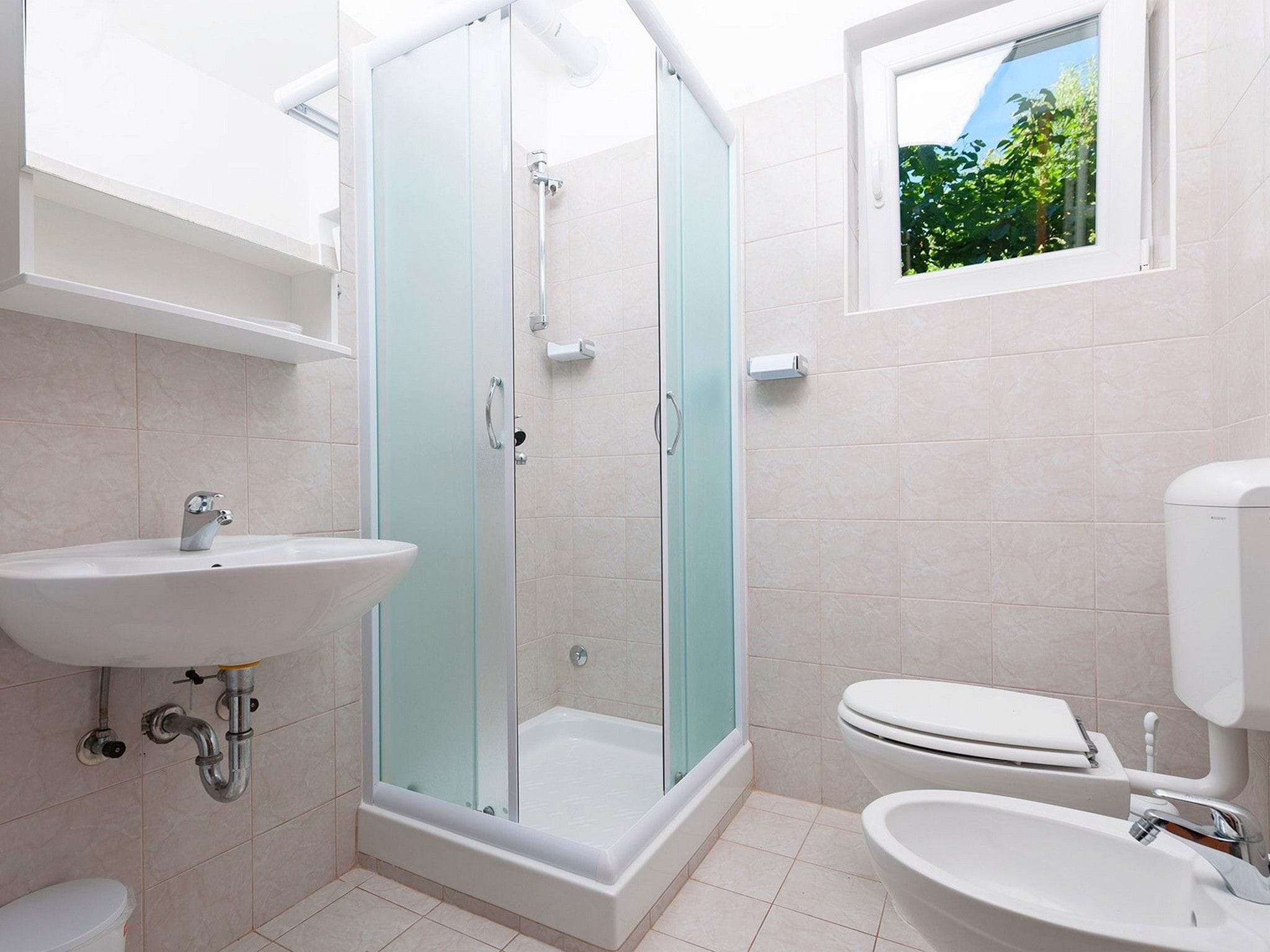Ein Badezimmer mit Duschkabine, Waschbecken, Toilette und einem Fenster mit Blick ins Grüne.