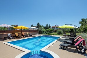 Una piscina con sillas de descanso y sombrillas, rodeada de una valla de madera y vegetación.