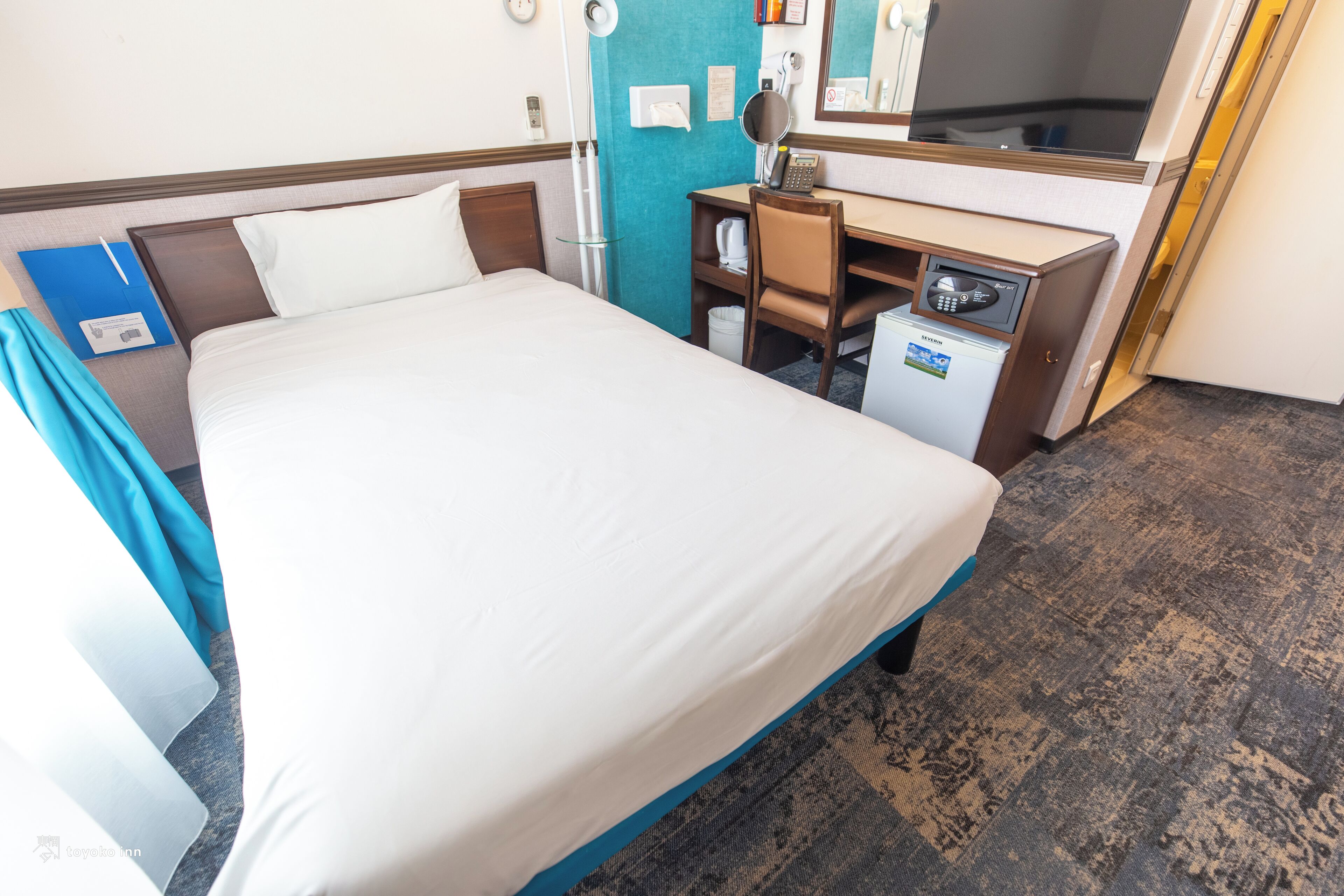 Quarto de hotel com cama grande, escrivaninha com computador, pequeno frigorífico e espelho.