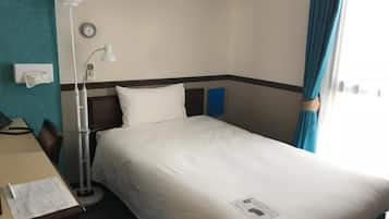 Una camera d'albergo con un letto, una scrivania con lampada, una sveglia al muro e una finestra con tende.