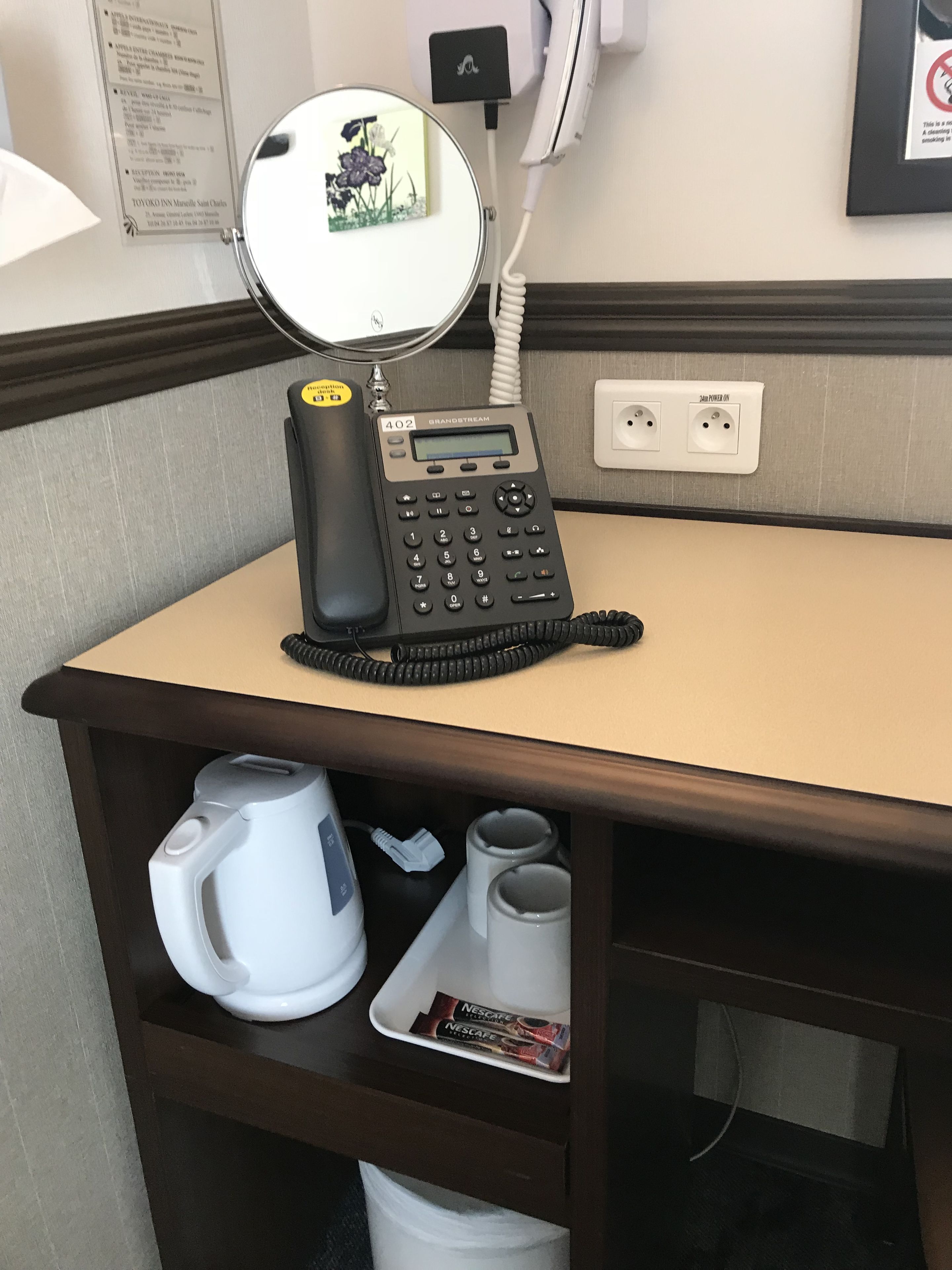 A hotel reception desk with a Grandstream phone, a coffee maker, and a Nescafe coffee pod.