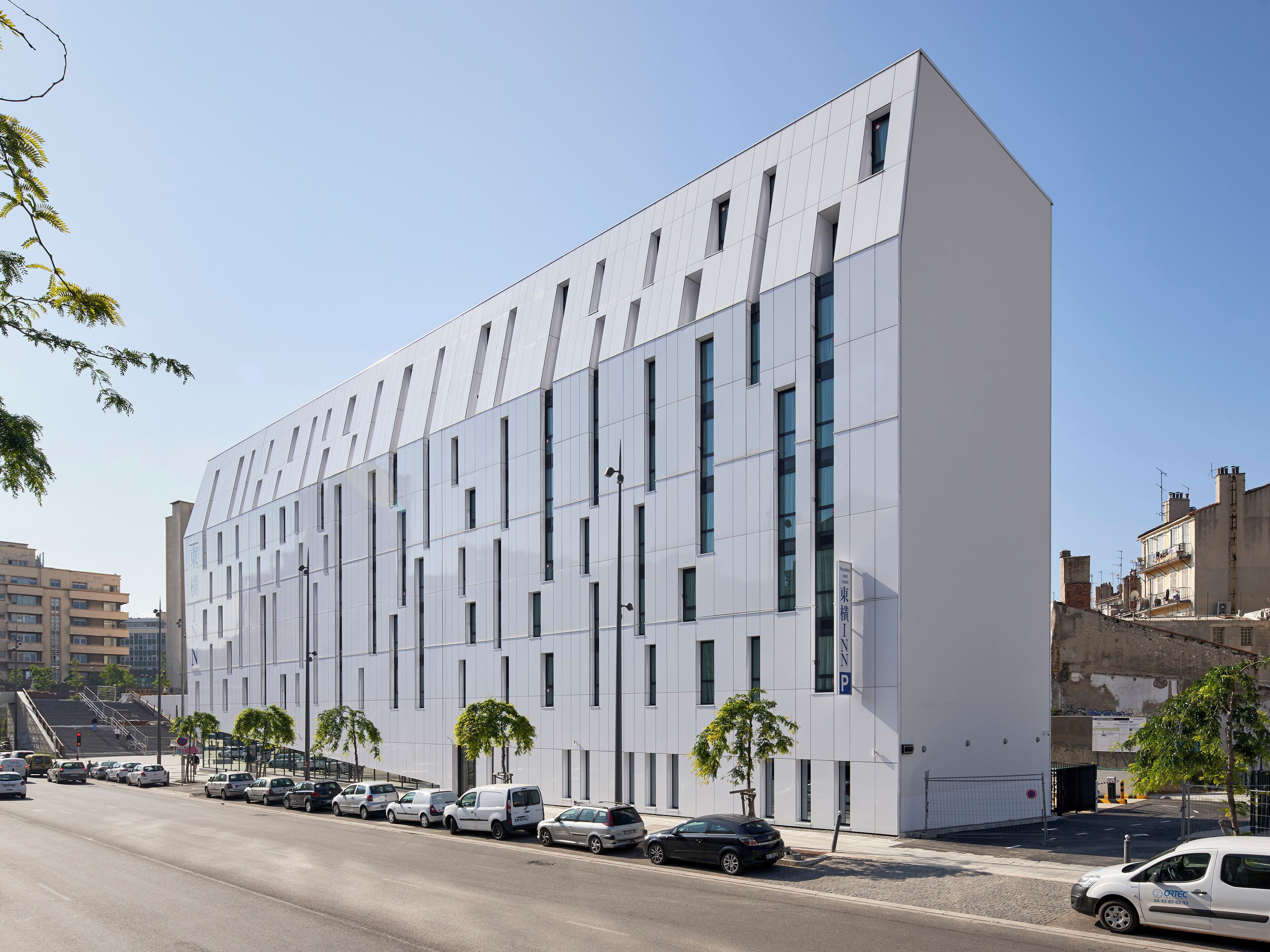 A modern building with a white facade, multiple windows, and a parking lot with cars.
