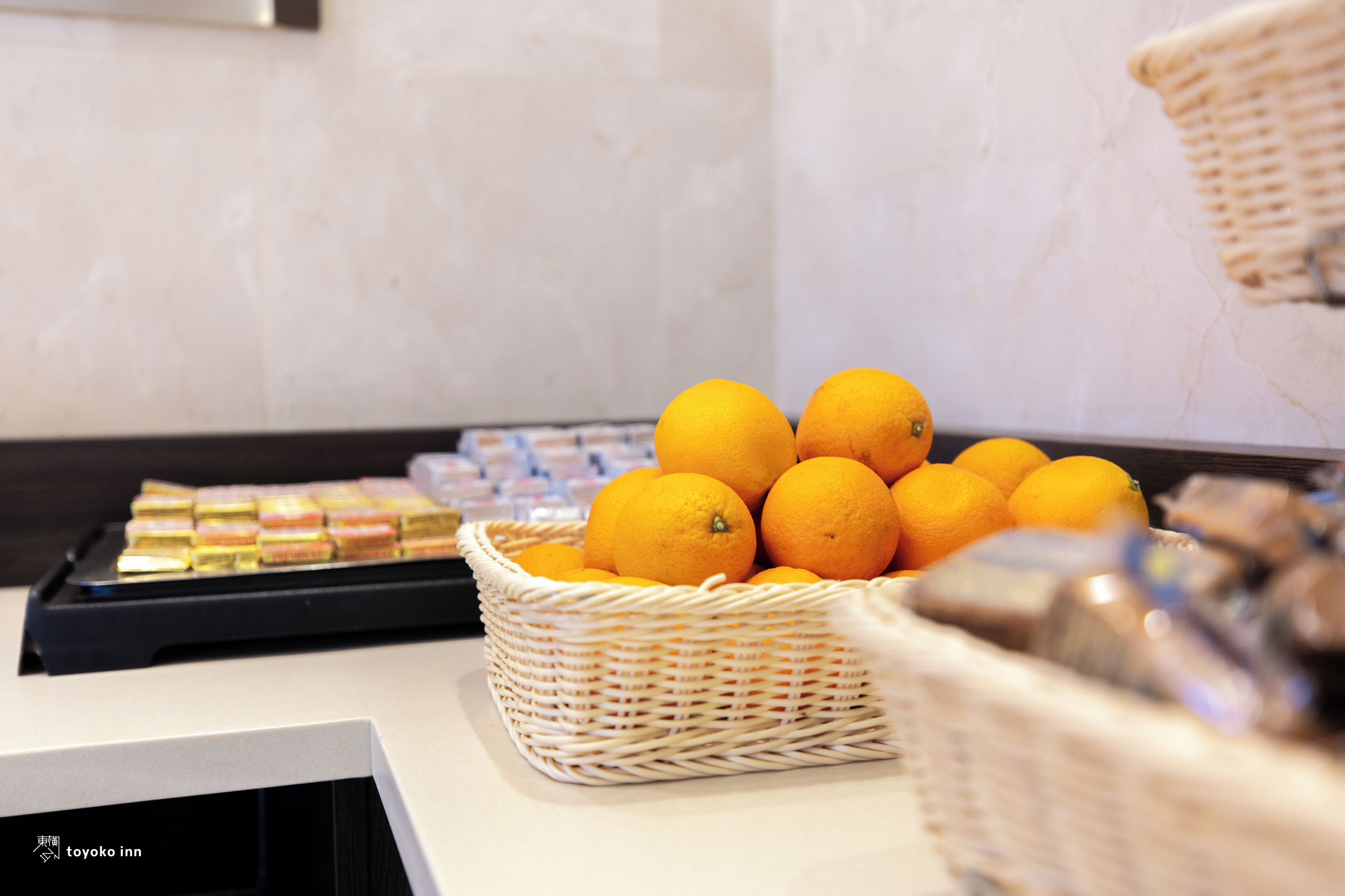 A buffet table with a wicker basket filled with oranges and a tray of pastries.