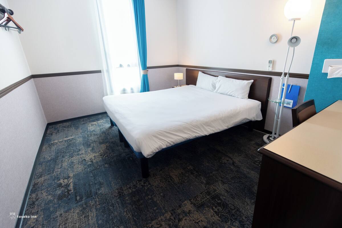 Una camera d'albergo con un letto, un comodino, una lampada e vista sull'esterno.