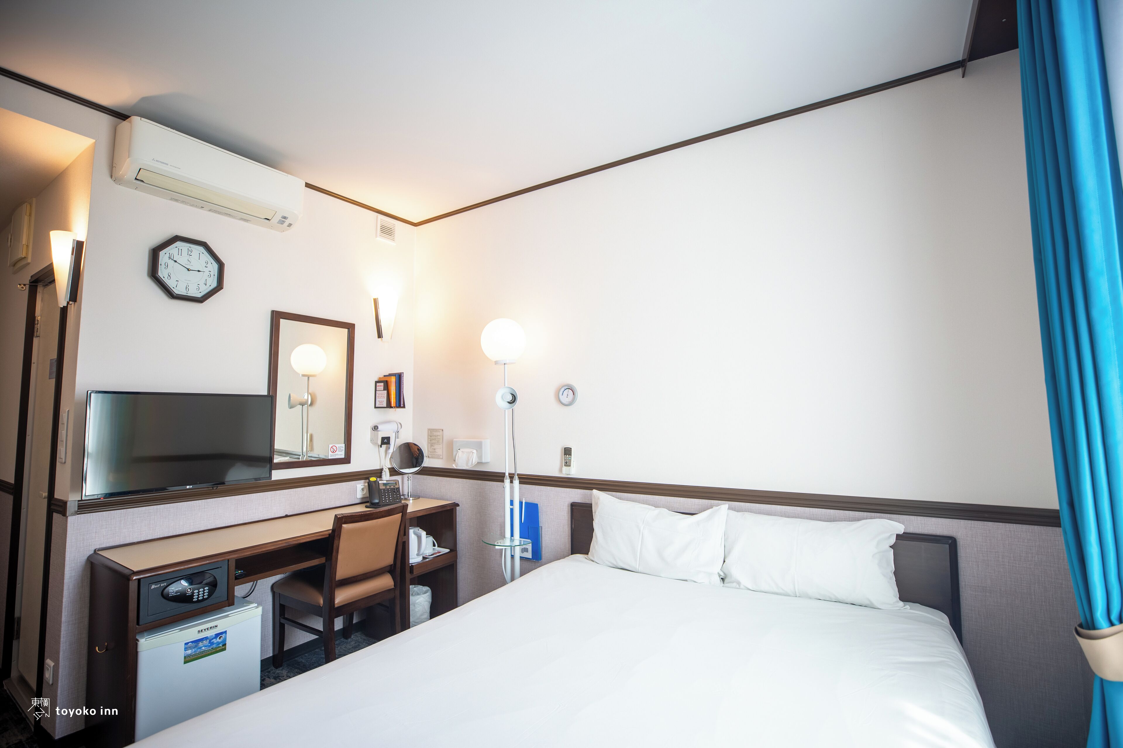 A hotel room with a bed, desk, chair, and a television.